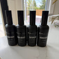 Four black bottles with labels on a white surface near a window