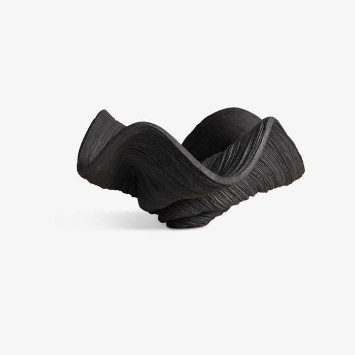Small coiled black porcelain bowl with a dynamic wavy shape and intricate horizontal lines on a white background