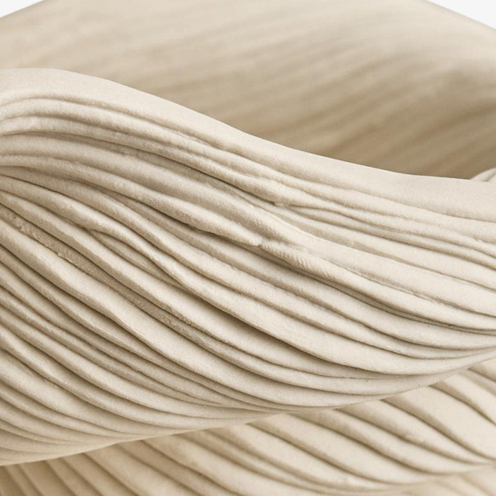 Close-up of a coiled beige porcelain small bowl showing the wavy horizontal ridges of the material