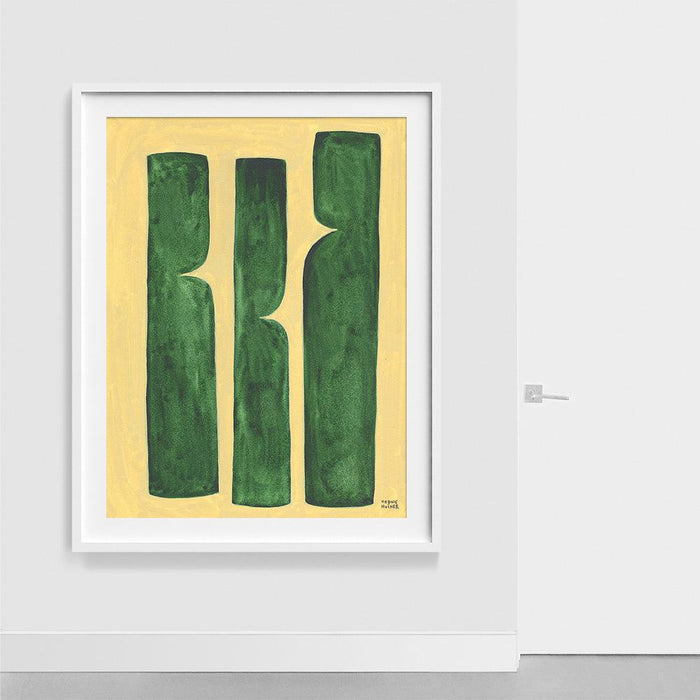 Framed abstract print with three green vertical shapes on yellow hanging on a white wall next to a white door